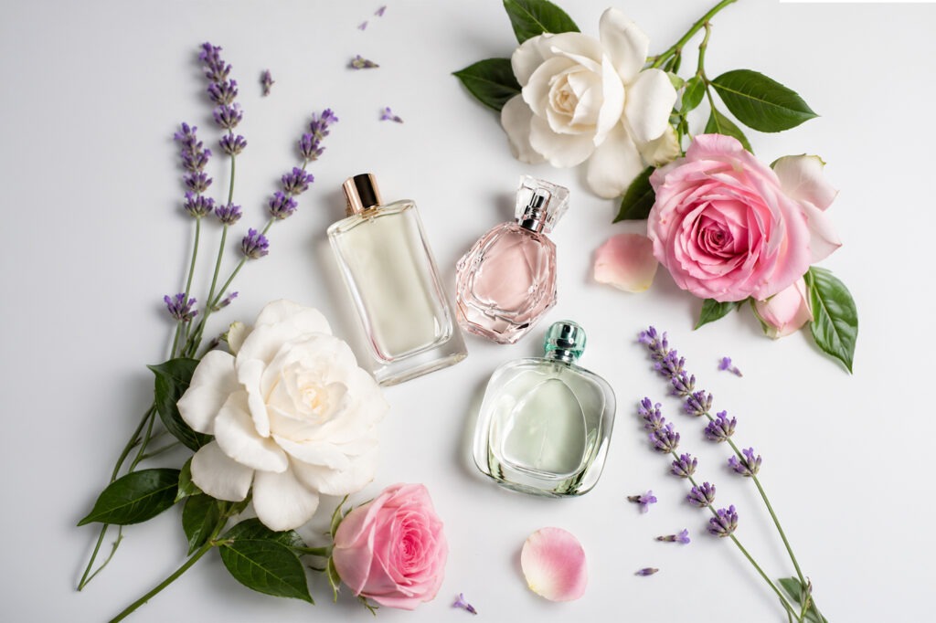 Three elegant perfume bottles are arranged among blooming roses and sprigs of lavender on a soft background, highlighting fragrance and beauty.